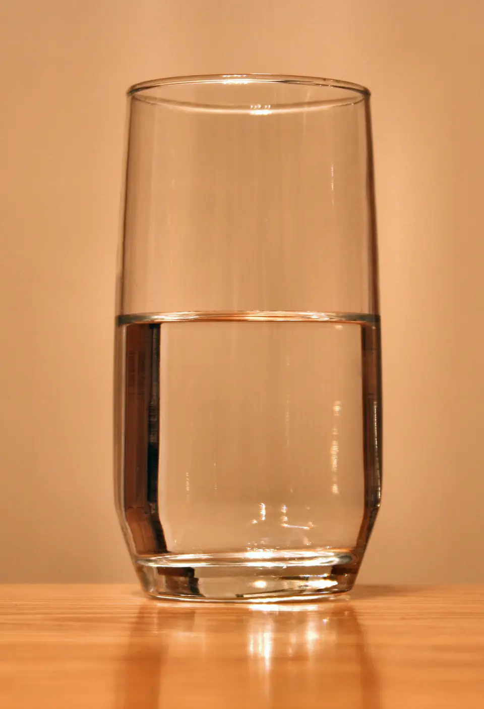 Vaso de vidrio con agua hasta la mitad sobre una mesa de madera