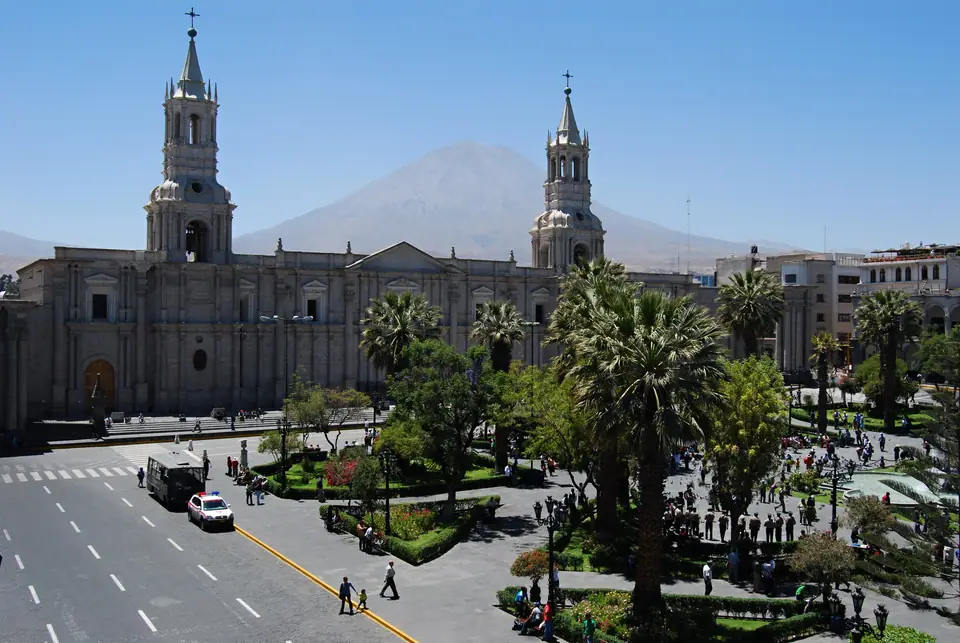 Plaza de Armas de Arequipa con la catedral y palmeras, y un volcán de fondo bajo cielo azul