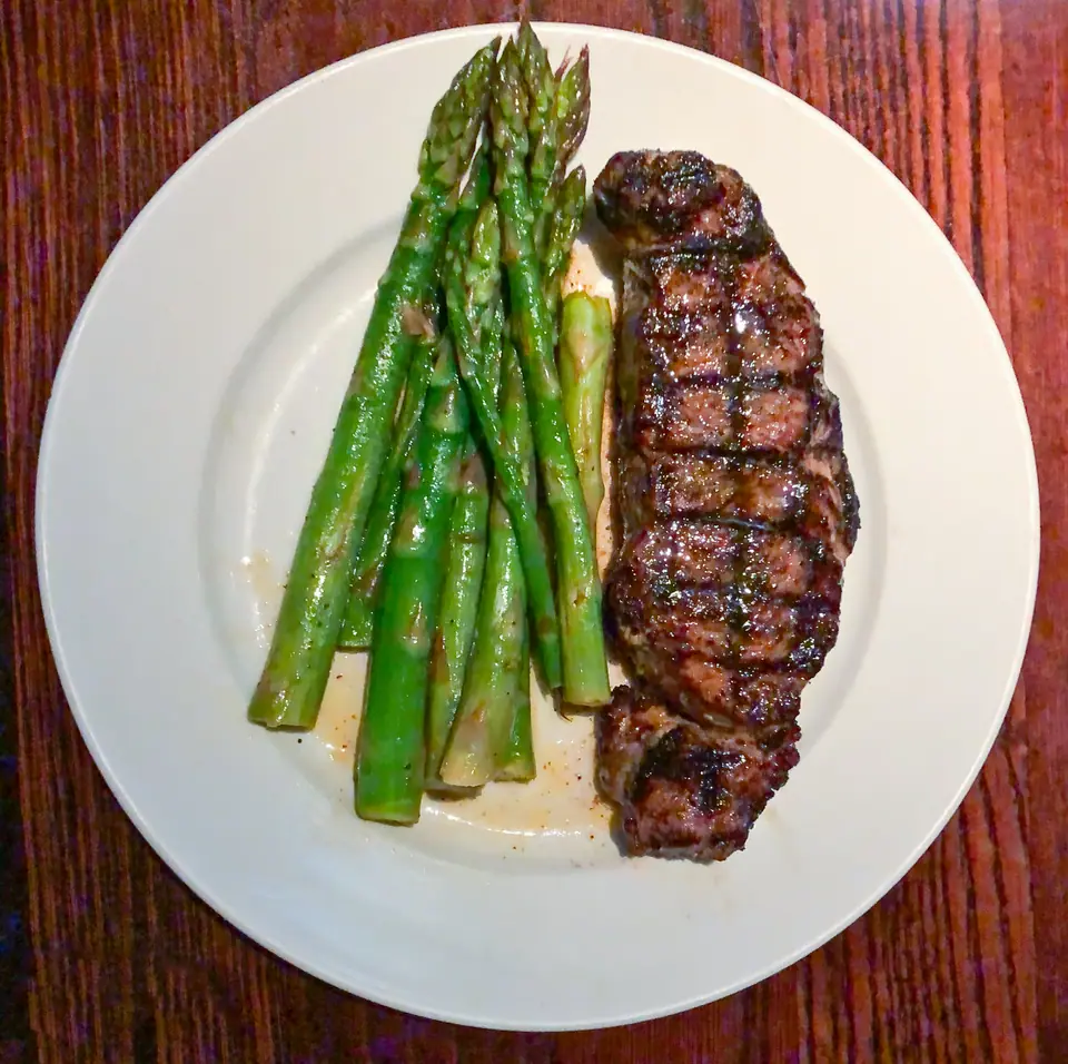 Bife de chorizo a la parrilla con marcas de grill, servido con espárragos en un plato blanco
