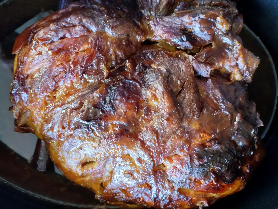 Paleta de cerdo asada, dorada y brillante, en una fuente oscura