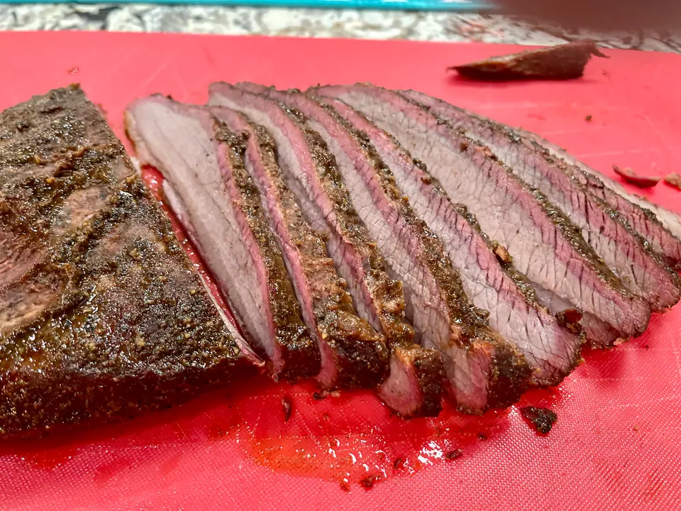 Brisket ahumado cortado en fetas sobre una tabla, con la corteza oscura