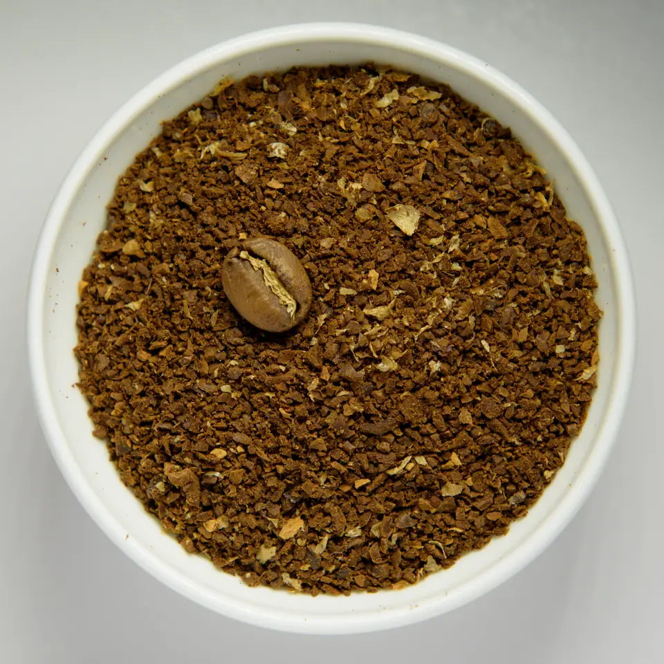Bol blanco con café molido grueso y un grano tostado entero encima