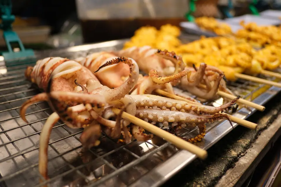 Calamares enteros a la parrilla, ensartados en pinchos, sobre la plancha de un puesto callejero