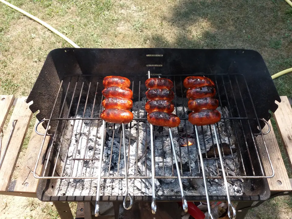Chorizos frescos cocinándose sobre la parrilla de un asador a carbón