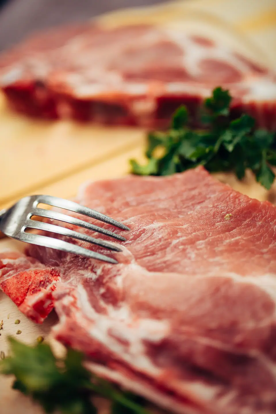 Chuletas de cerdo crudas con hueso sobre una tabla, con perejil fresco