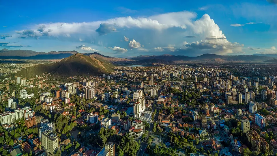 Vista aérea de Cochabamba con edificios, un cerro verde y nubes al fondo