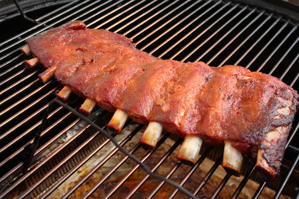 Tira de costillas de cerdo dorada asándose sobre la parrilla