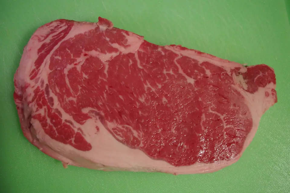 Bife de carne vacuna cruda y marmolada sobre una tabla de cortar verde