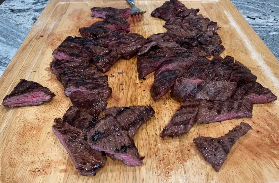 Entraña asada cortada en trozos sobre una tabla de madera, con marcas de parrilla y centro rosado