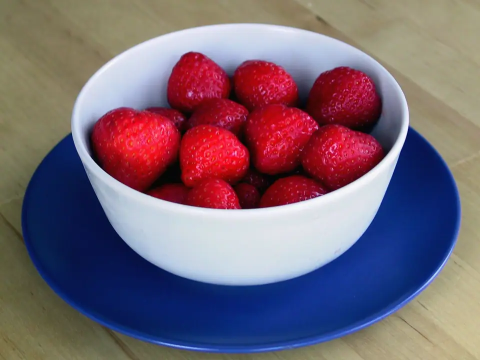 Bol blanco lleno de frutillas enteras sobre un plato azul