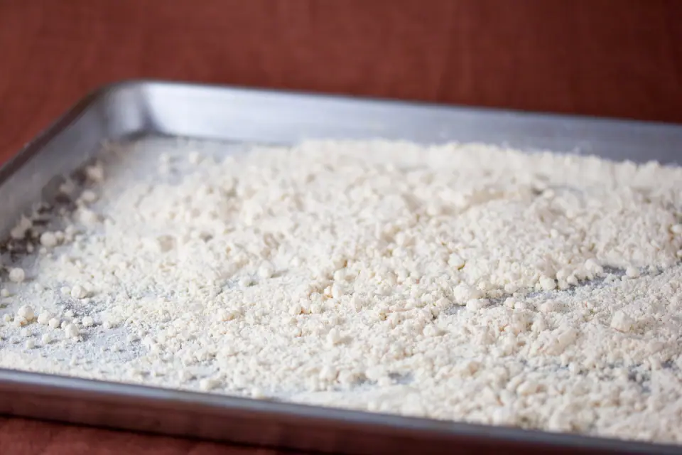 Harina de coco clara extendida en una bandeja metálica para horno