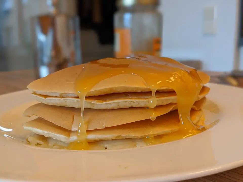 Pila de panqueques esponjosos con miel chorreando, en un plato blanco