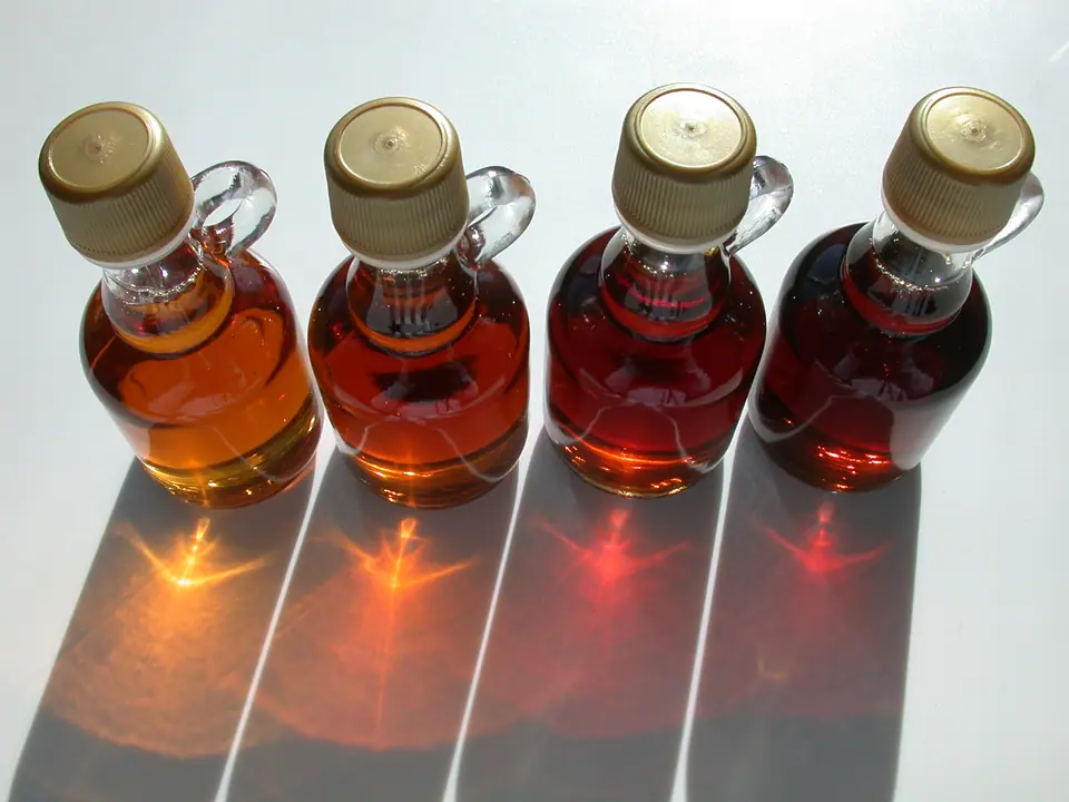 Cuatro botellas de jarabe de arce en tonos de ámbar claro a oscuro, a contraluz