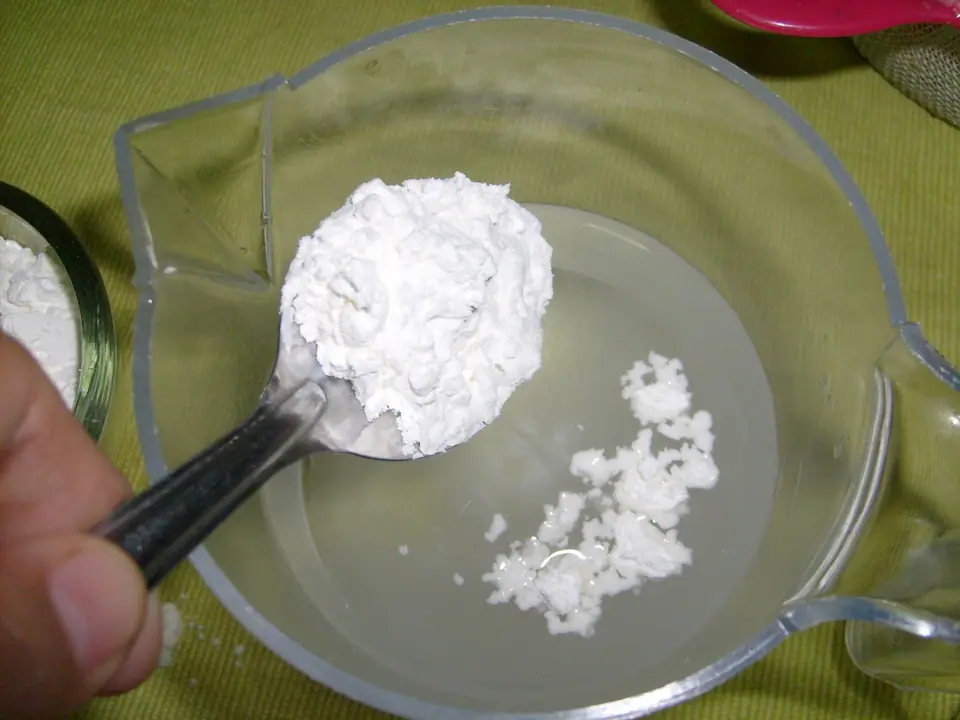 Cuchara con fécula de maíz en polvo sobre una jarra con agua, para disolverla