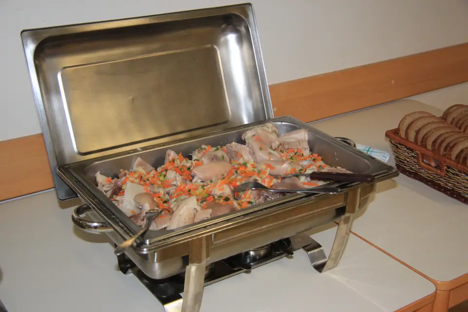 Fuente de buffet de acero inoxidable con la tapa levantada y comida adentro, sobre su soporte para mantenerla caliente