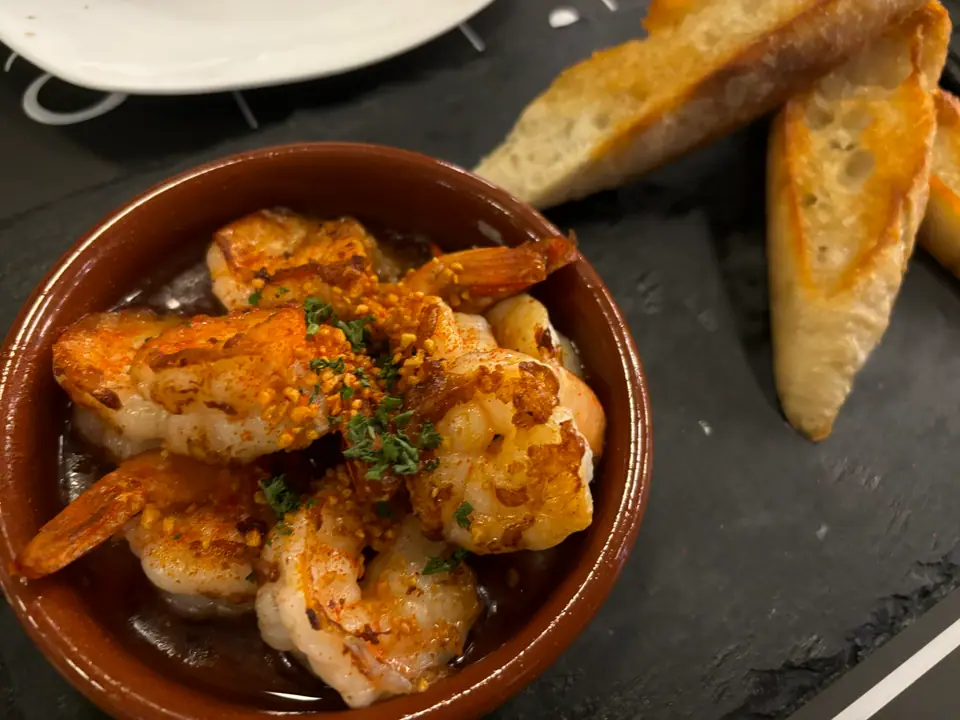 Cazuela de barro con camarones salteados, junto a rodajas de pan tostado