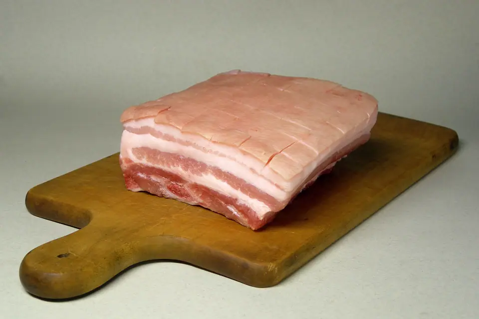Pieza de panza de cerdo cruda, con capas de grasa y carne, sobre una tabla de madera