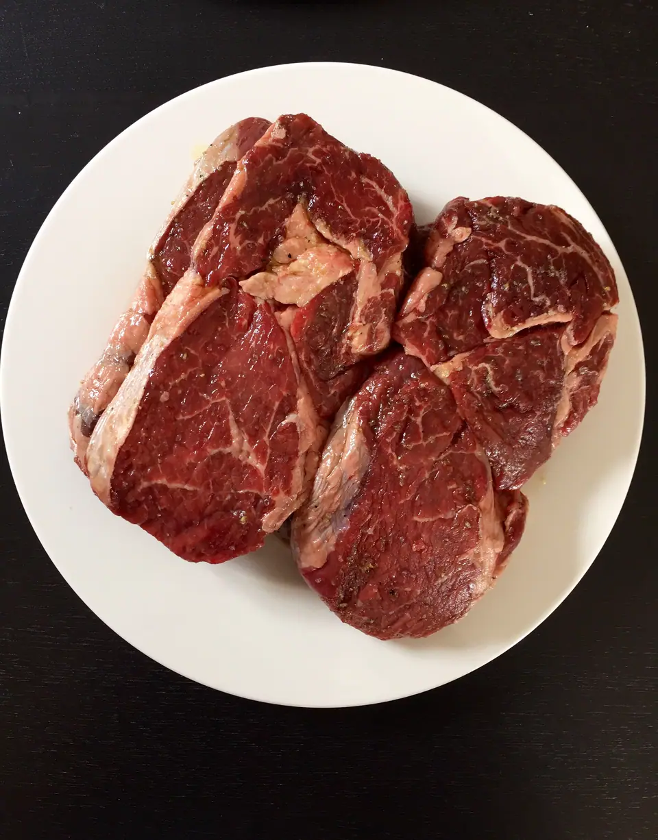 Bifes de ojo de bife crudos y marmoleados en un plato blanco