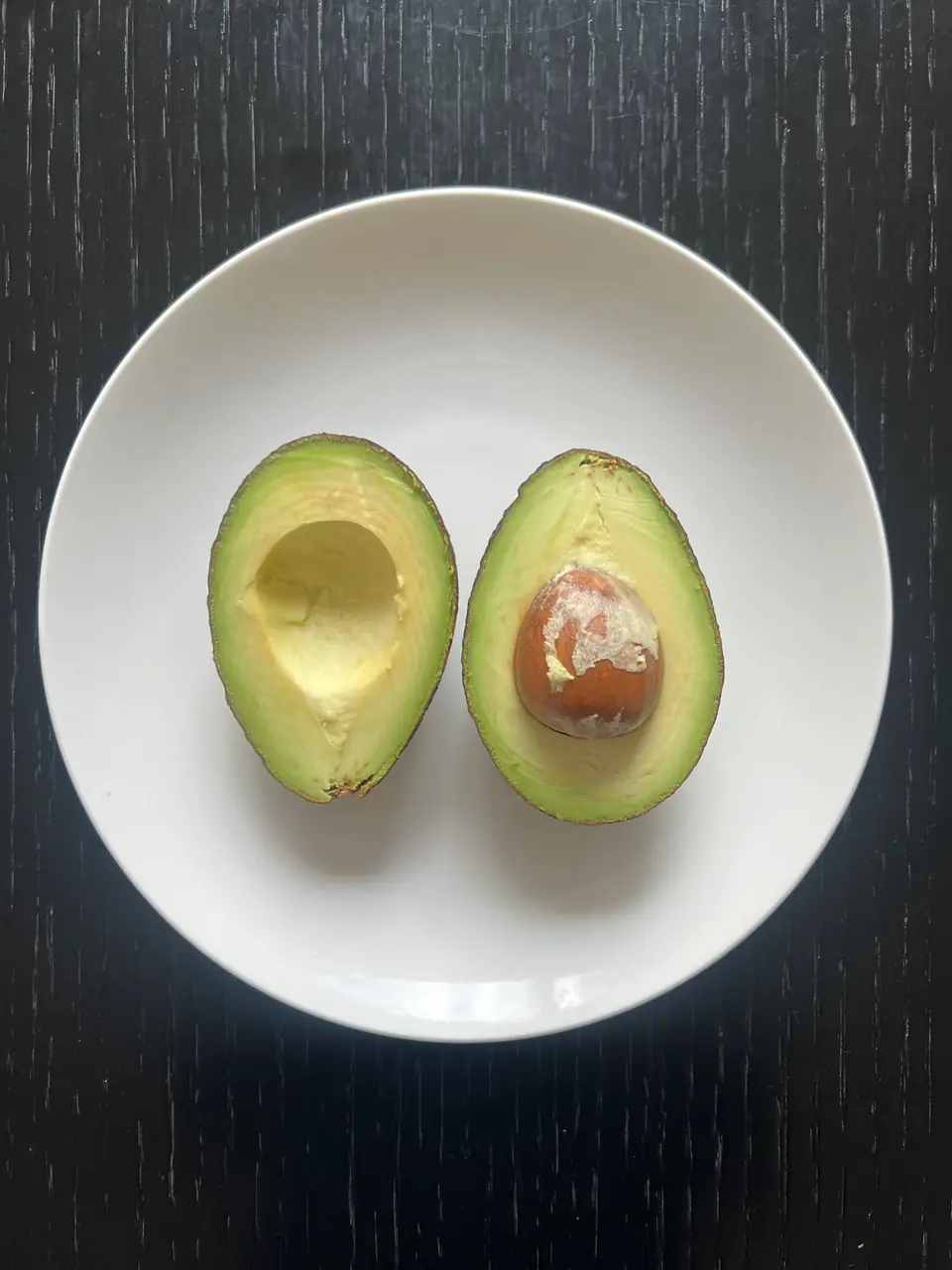 Palta cortada al medio en un plato blanco, una mitad con el carozo