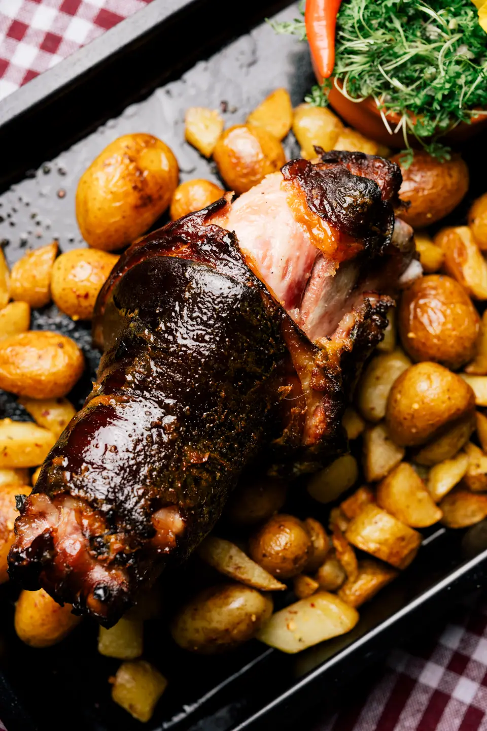 Pierna de cerdo asada con la piel dorada, en una bandeja con papas