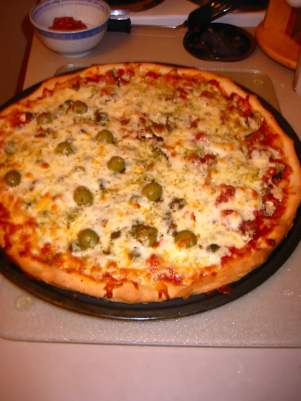 Pizza casera redonda de muzzarella con aceitunas verdes recién salida del horno