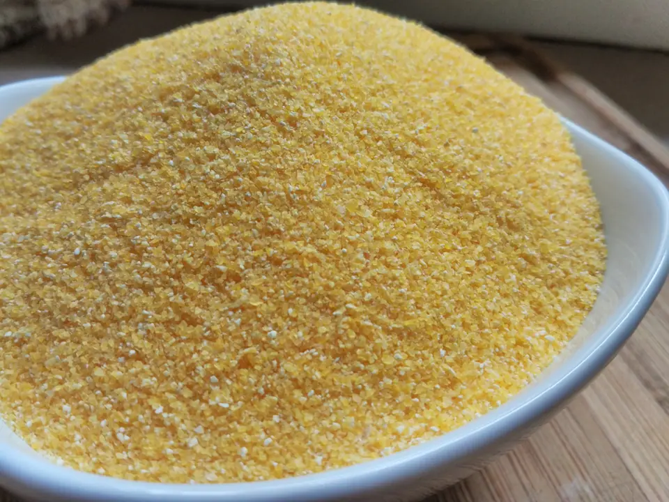Bol blanco lleno de polenta cruda, harina de maíz amarilla de grano fino