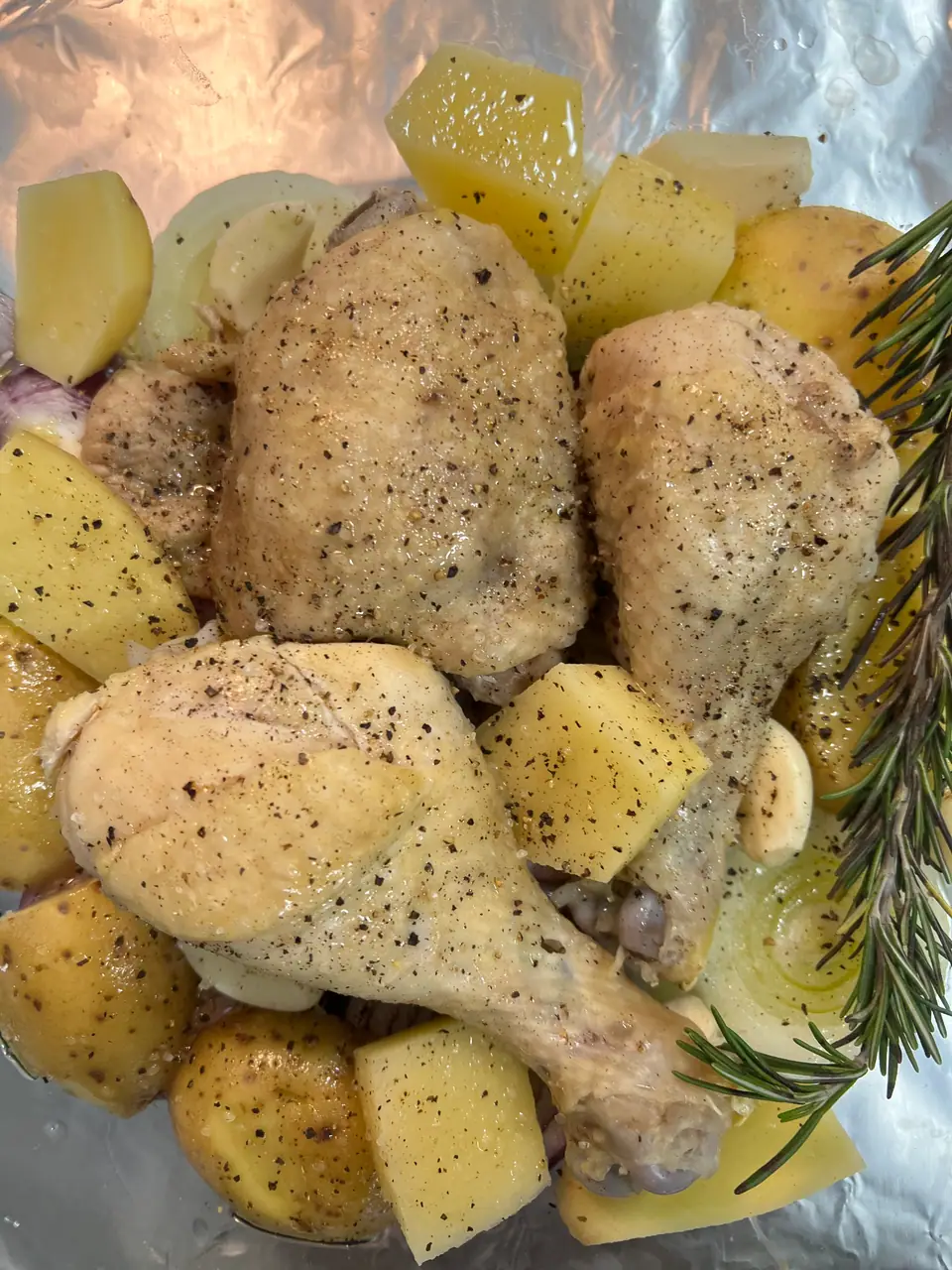 Presas de pollo, muslos y patas, condimentadas con pimienta junto a papas en papel de aluminio