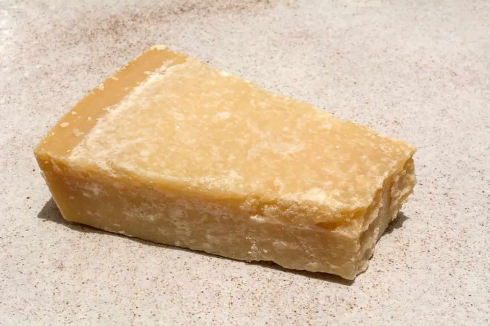 Trozo en cuña de queso duro tipo parmesano sobre una superficie clara