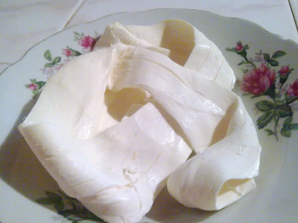 Queso Oaxaca blanco desenrollado en tiras anchas sobre un plato con flores