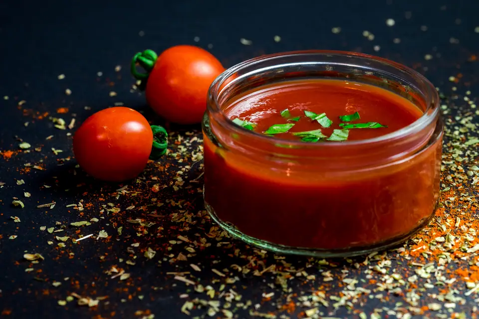 Frasco de vidrio con salsa de tomate y tomates frescos al lado
