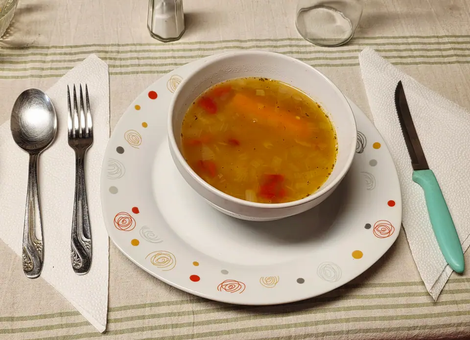 Tazón de sopa de verduras con zanahoria y morrón, servido en la mesa con cubiertos