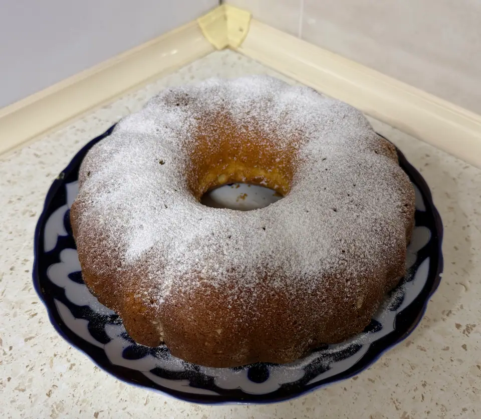 Torta casera en molde de corona espolvoreada con azúcar impalpable, sobre un plato azul
