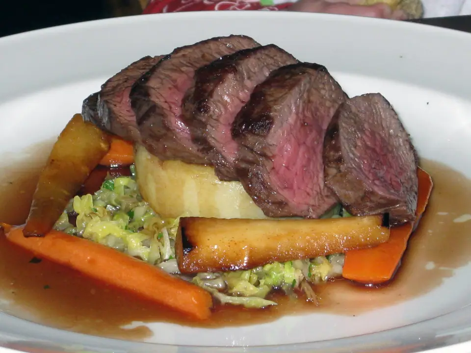 Lomo de venado asado cortado en fetas, rosado por dentro, con verduras y salsa