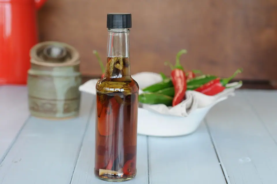 Botella de vidrio con vinagre saborizado con ajíes, junto a un bol de ajíes frescos