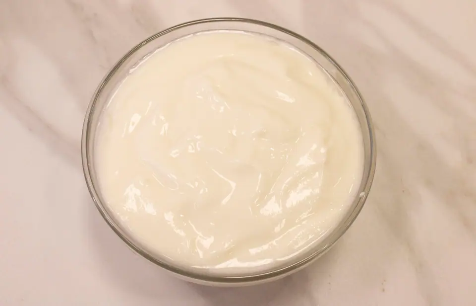 Bol de vidrio con yogur natural cremoso sobre una mesada clara